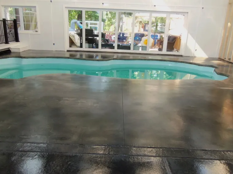 Dark stained and sealed concrete deck around an indoor swimming pool